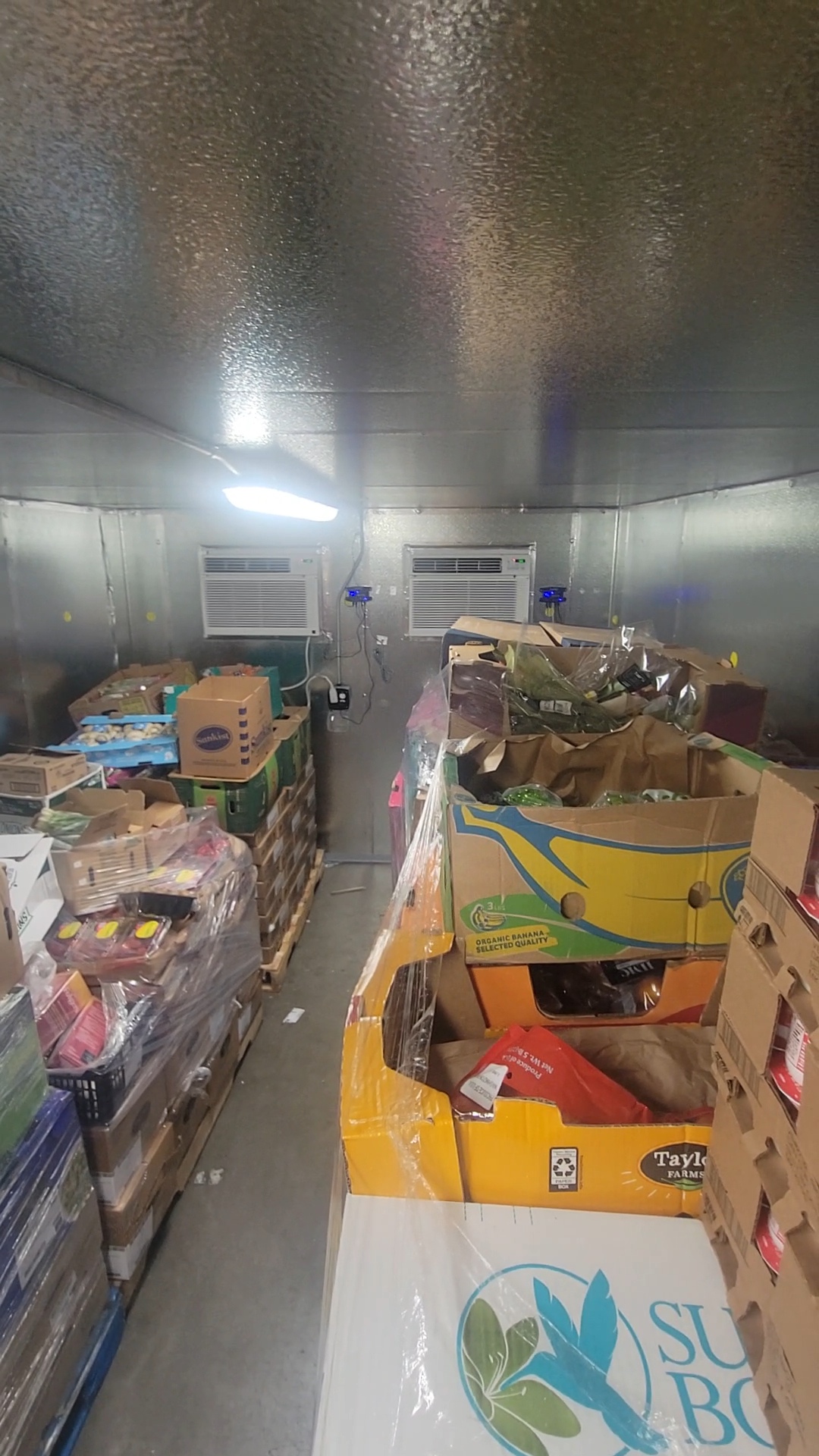 Box fridge unit full of pallets of boxed produce in plastic wrap.